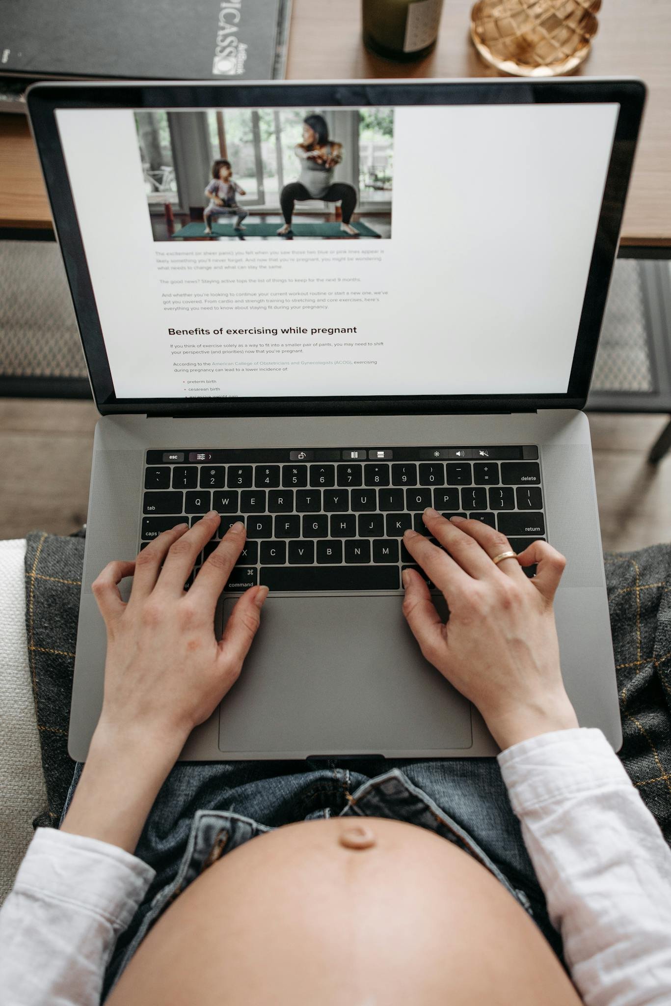 A pregnant woman uses a laptop, reading about pregnancy exercises from a top view.