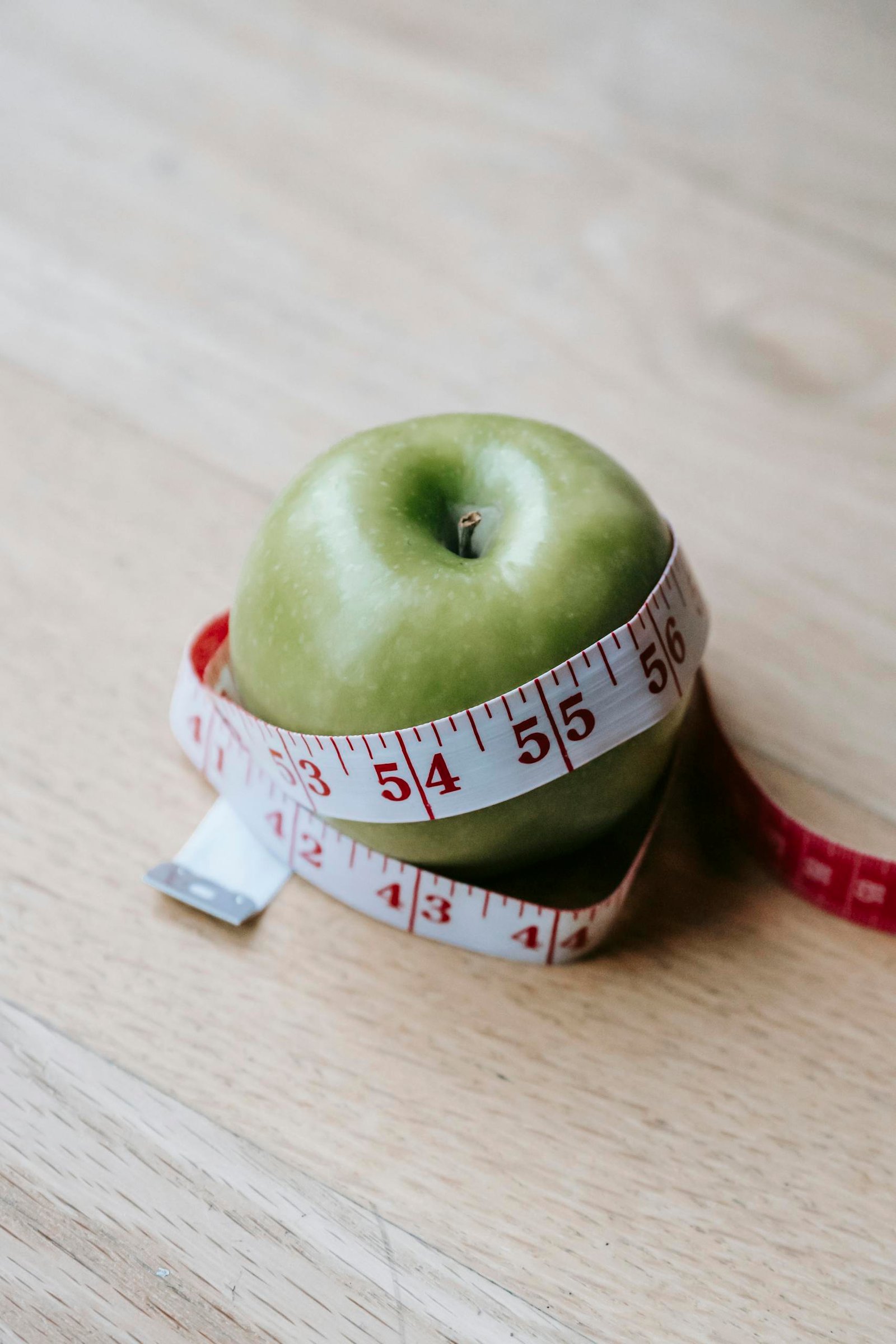A green apple encircled by a measuring tape, symbolizing diet and fitness goals.