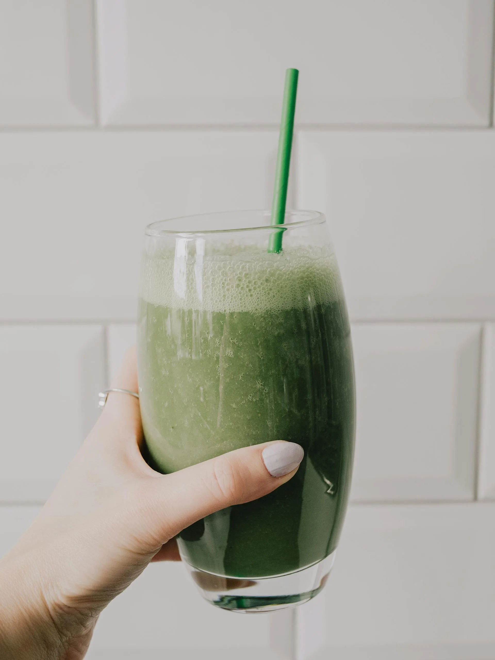 A hand holding a vibrant green smoothie with a straw, showcasing a healthy lifestyle.