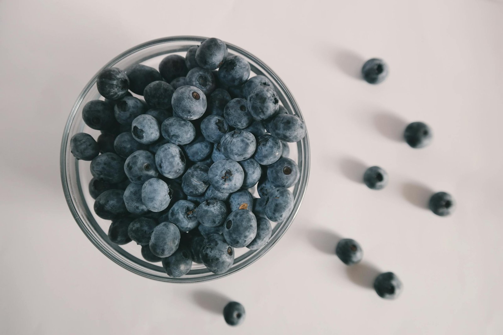 A top view of fresh blueberries spilling from a glass bowl on a white background, showcasing vibrant colors.