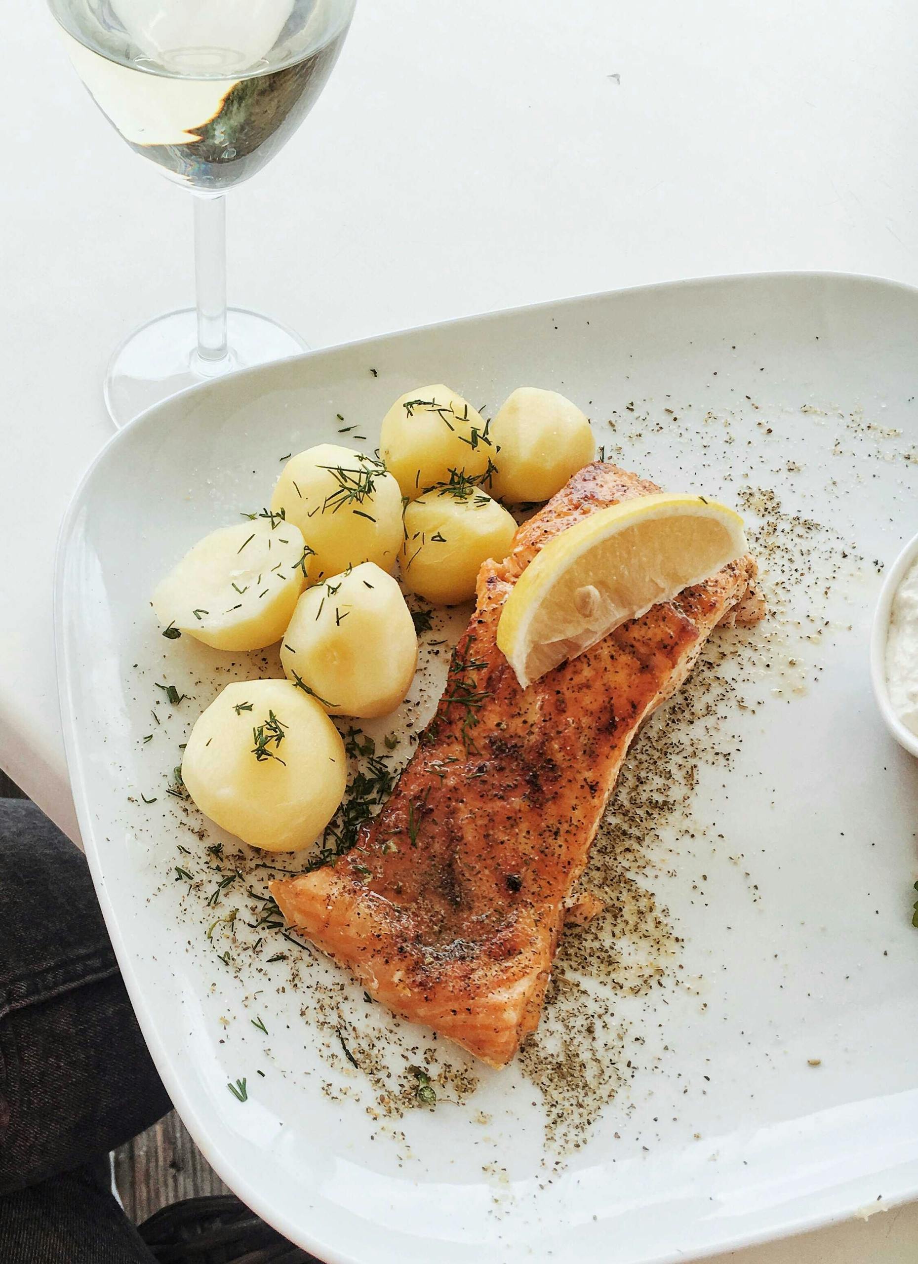 Close-up of baked salmon with potatoes, herbs, and lemon slice on a ceramic plate.