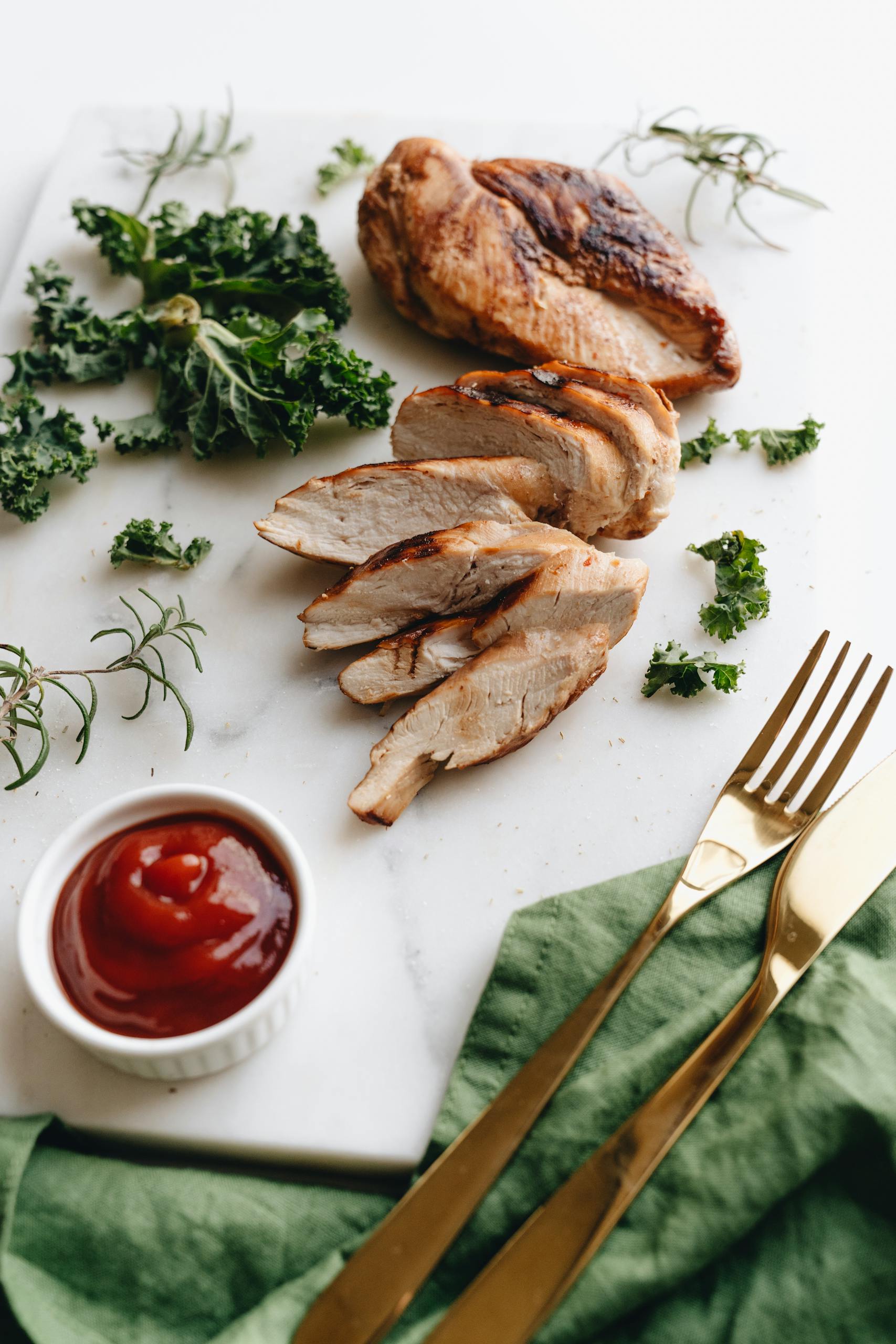 Delicious sliced grilled chicken breast with kale and ketchup on a marble board, styled for a top-down view.