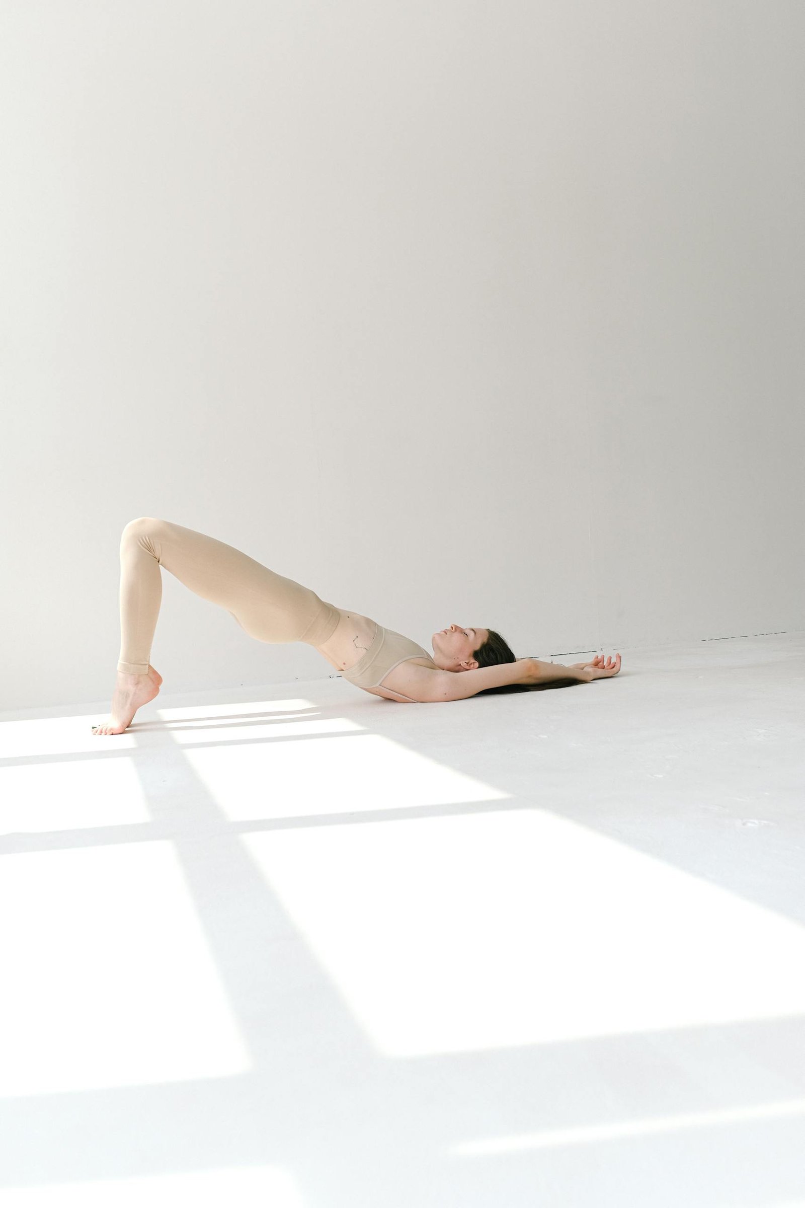 Full-length shot of a woman striking a bridge pose in a sunlit studio, emphasizing fitness and tranquility.