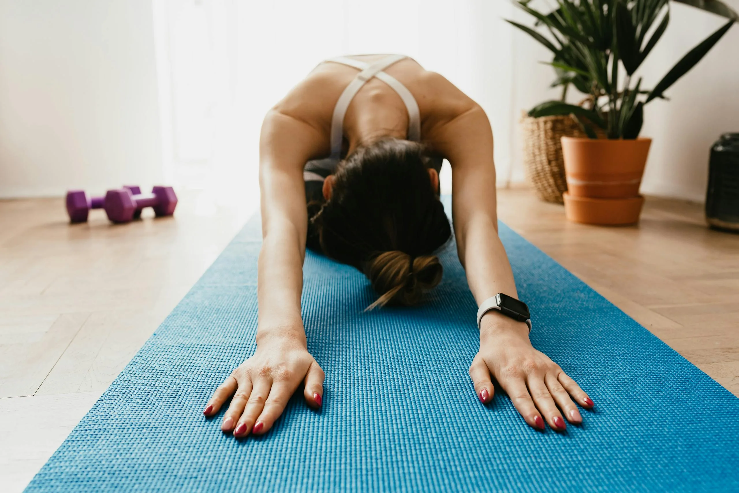 Woman doing a child's pose on a blue yoga mat at home, promoting fitness and wellbeing.