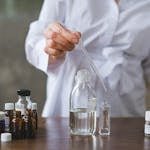 Scientist using a dropper to mix liquids in glass bottles, showcasing a laboratory setting.